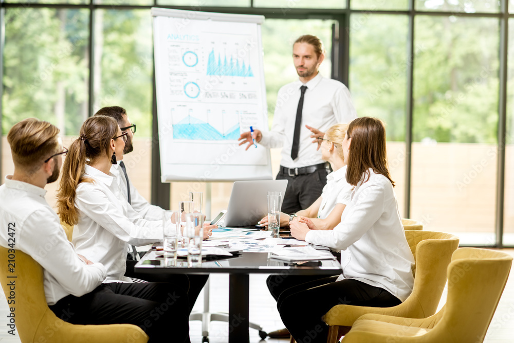 Fototapeta premium Handsome speaker reporting with flip chart during a business conference with partners sitting at the table in the office
