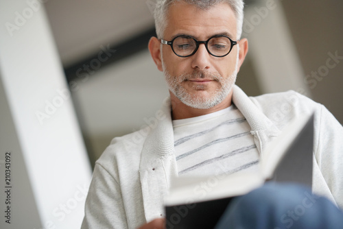 Trendy mature guy with eyeglasses reading book at home photo