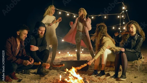 girl seduces guys with erotic dances at evening picnic and broil sausages, friends at camping party