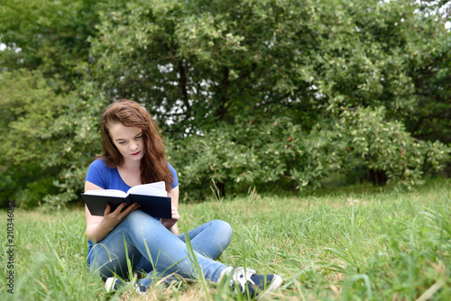 Casual student sitting in a park reading a book