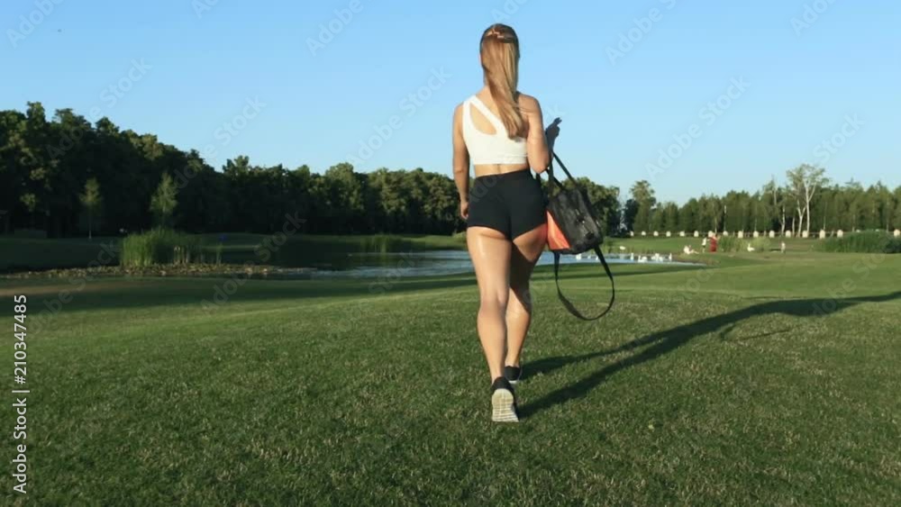 Sporty woman walking in the city park. View from back. Sporty woman walking in the city park. View from back.