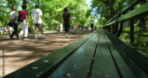 A slow left-to-right dolly establishing shot of the iconic green benches of Central Park with unidentifiable tourists walk on The Mall in the background. Shallow depth of field.  	