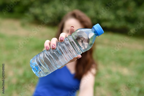 Fit girl showing a bottle of water to the camera sitting in a park