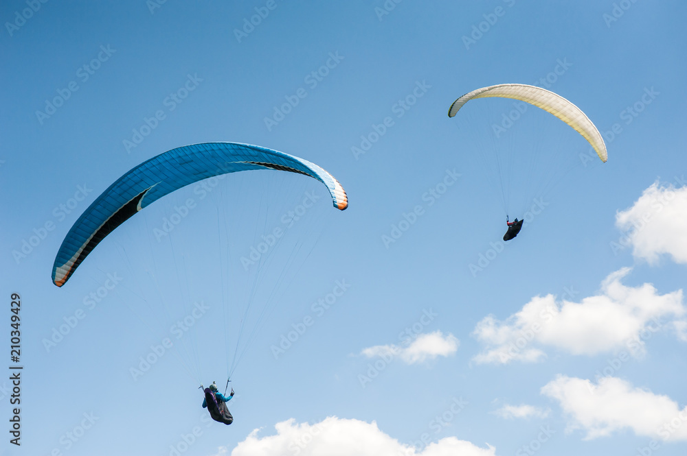 Two paragliders flying in the blue sky against the background of clouds. Paragliding in the sky on a sunny day. Two paragliders flying in the blue sky against the background of clouds. Paragliding in the sky on a sunny day.