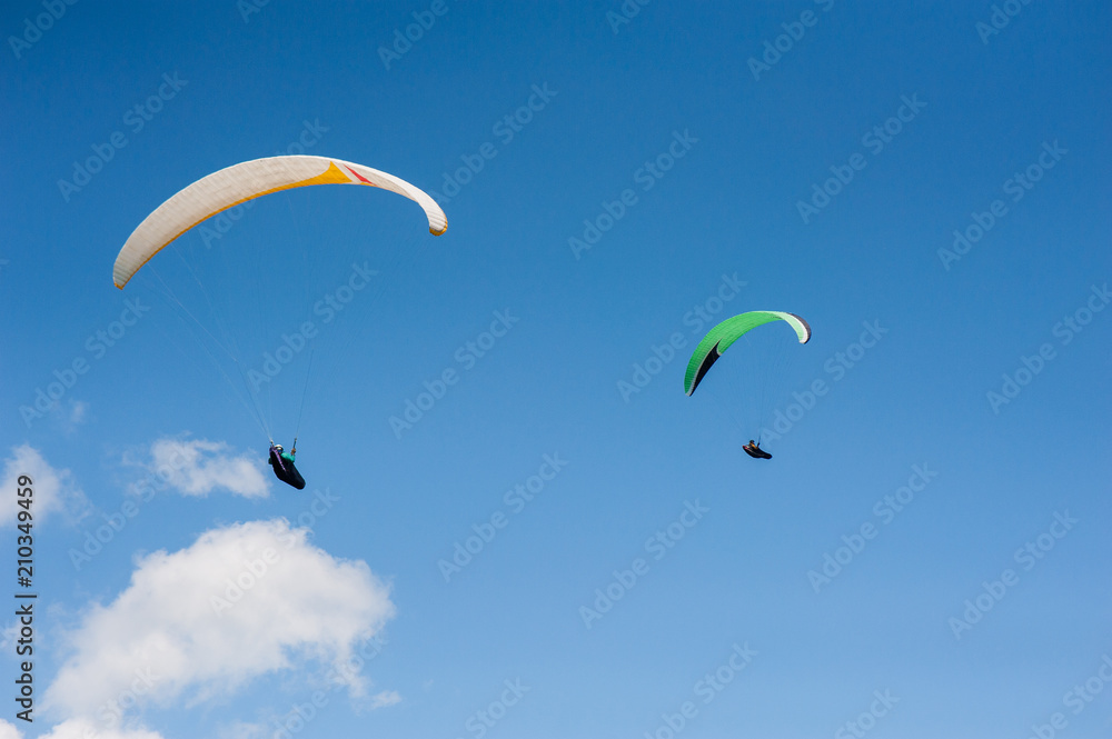 Two paragliders flying in the blue sky against the background of clouds. Paragliding in the sky on a sunny day. Two paragliders flying in the blue sky against the background of clouds. Paragliding in the sky on a sunny day.