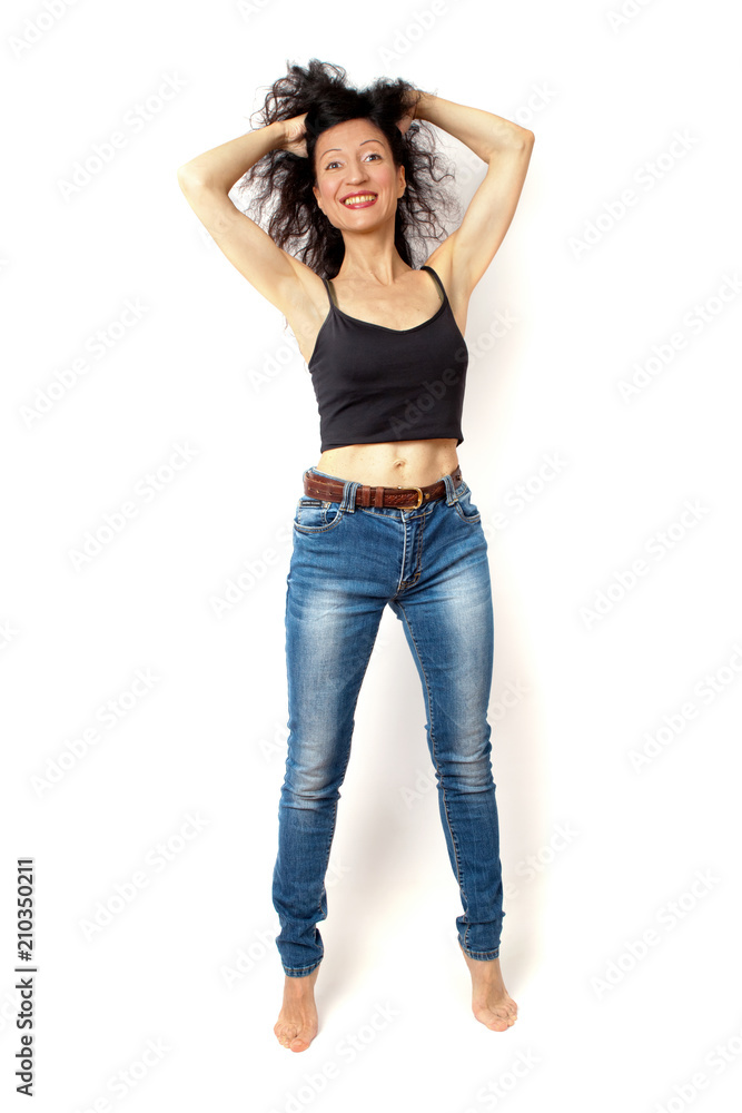 Cheerful slim curly brunette woman standing in blue jeans and a black shirt on a white background Cheerful slim curly brunette woman standing in blue jeans and a black shirt on a white background