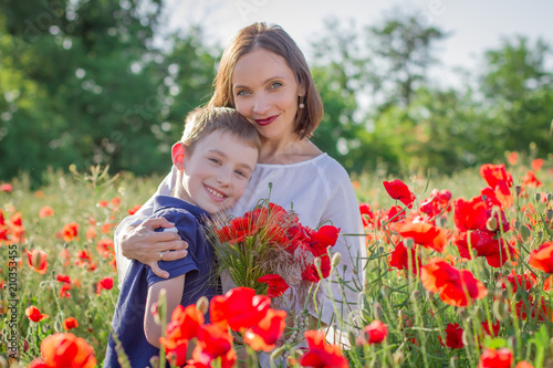 Mother in white with son holding bouquet on blossoming red poppies field © Angel_a