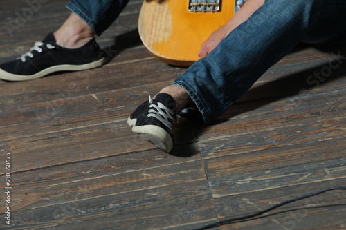 musician with a guitar sits on a wooden floor