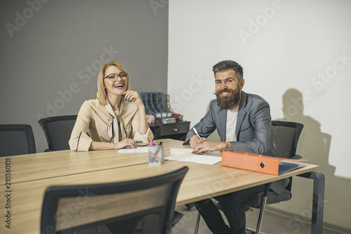Sensual woman and bearded man smile at business meeting. Happy business woman and man sit at office desk. Concentration at work. Communication and cooperation with colleagues. Work process concept