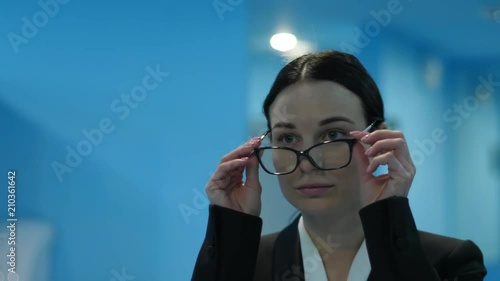 tired young woman in public restroom takes off her eyeglasses and unnerved looks at herself in the mirror