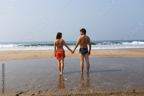 Beautiful young couple holding hands on the ocean shore. Sand beach. Gentle waves. Otpusuk at sea with a loved one. Romance.