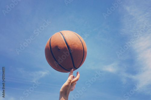 Spinning basketball on finger against summer sky background. Fun sport practice outside.