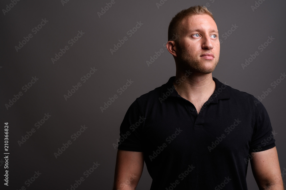 Man with blond hair wearing black polo shirt against gray backgr