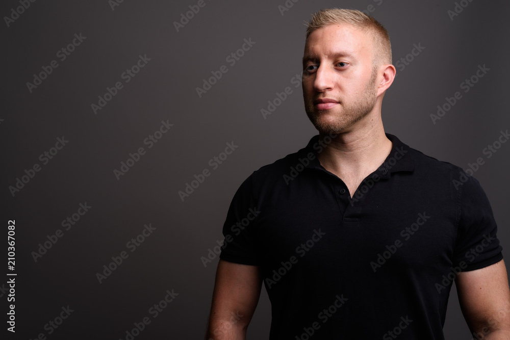 Naklejka premium Man with blond hair wearing black polo shirt against gray backgr