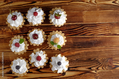 Nine cakes with protein cream and summer berries on wooden table. Black background, selective focus. Place for text, top view