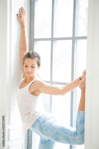 Young attractive woman practicing yoga. Working out wearing sportswear, white T-shirt and blue pants. Standing in Lord of the Dance exercise, Natarajasana pose