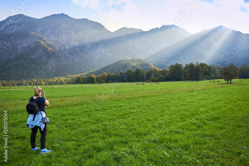 Ein Mädchen macht das Fotos von Bergen in den Alpen. Grünes Gras, Sommer und schöne Aussicht. © Trambitski