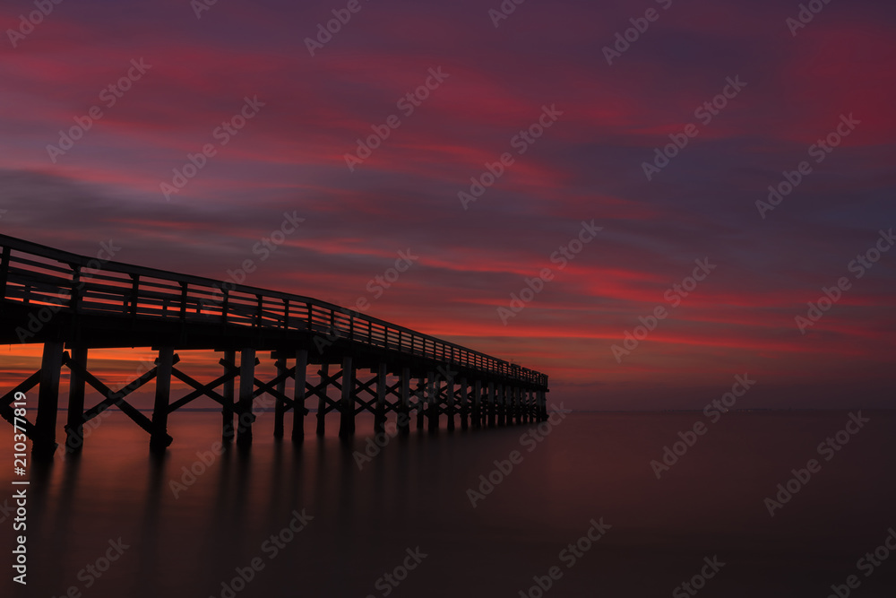 Dramatic red sunset viewed from Bayshore Waterfront Park, New Jersey featuring fishing pier on the background