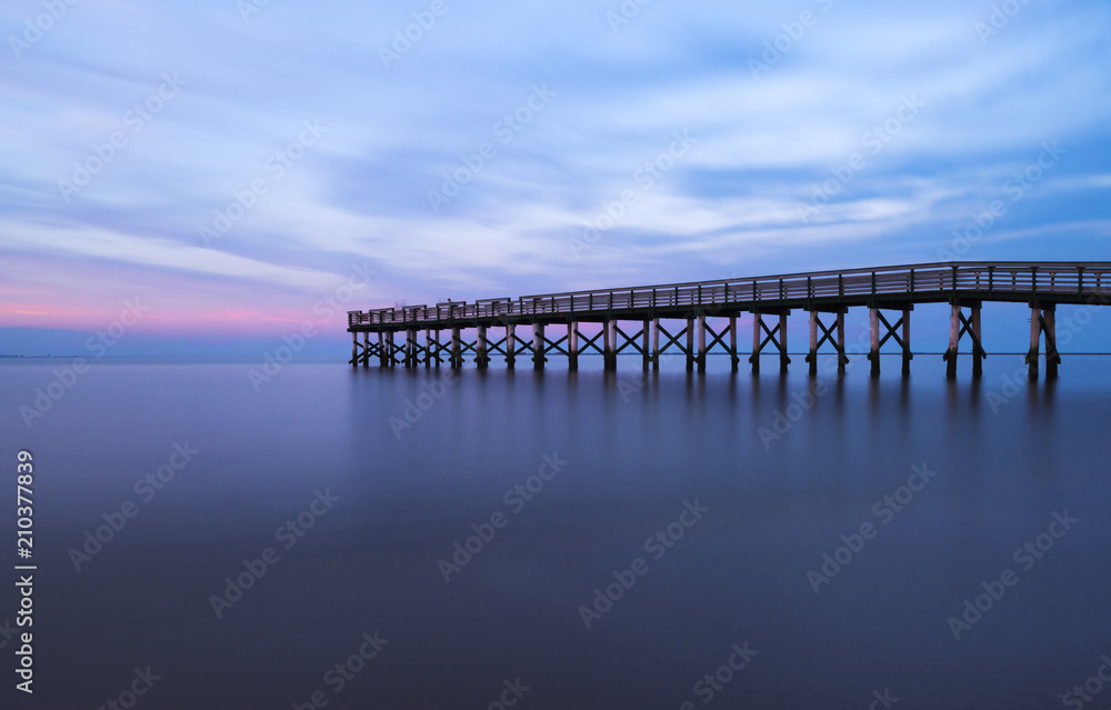 Peaceful sunset viewed from Bayshore Waterfront Park, New Jersey featuring fishing pier on the background using long exposure