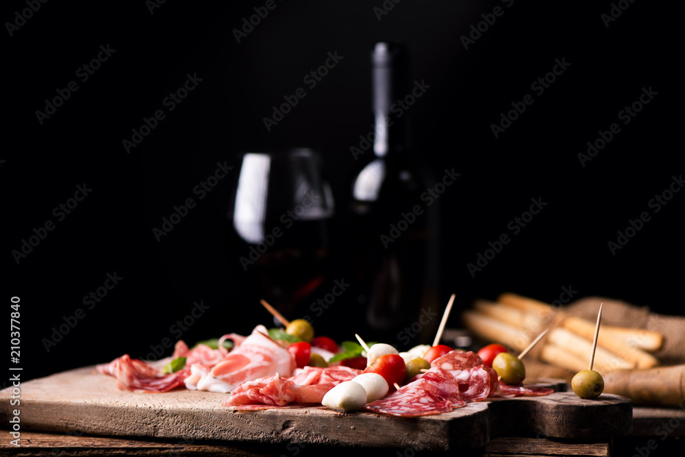 Assorted meats and  cherry mozzarella cheese, on a wooden cutting board with bottle of wine and glass on background. Italian antipasti