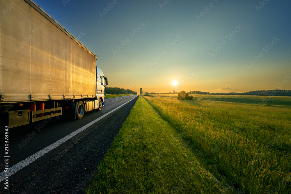 Truck driving on the asphalt road in a rural landscape in the golden sunset Truck driving on the asphalt road in a rural landscape in the golden sunset