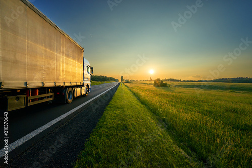 Obraz na płótnie Truck driving on the asphalt road in a rural landscape in the golden sunset w salonie
