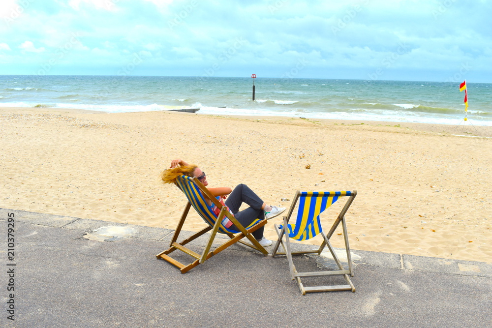 Blond girl sitting on a deck chair on the beach, Bournemouth, England, June Blond girl sitting on a deck chair on the beach, Bournemouth, England, June