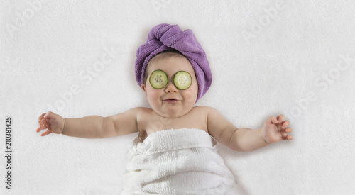 Funny baby girl wrapped in white towel with cucumbers on her eyes photo