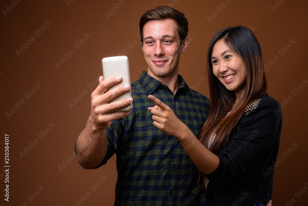 Studio shot of young multi-ethnic couple together against brown Studio shot of young multi-ethnic couple together against brown