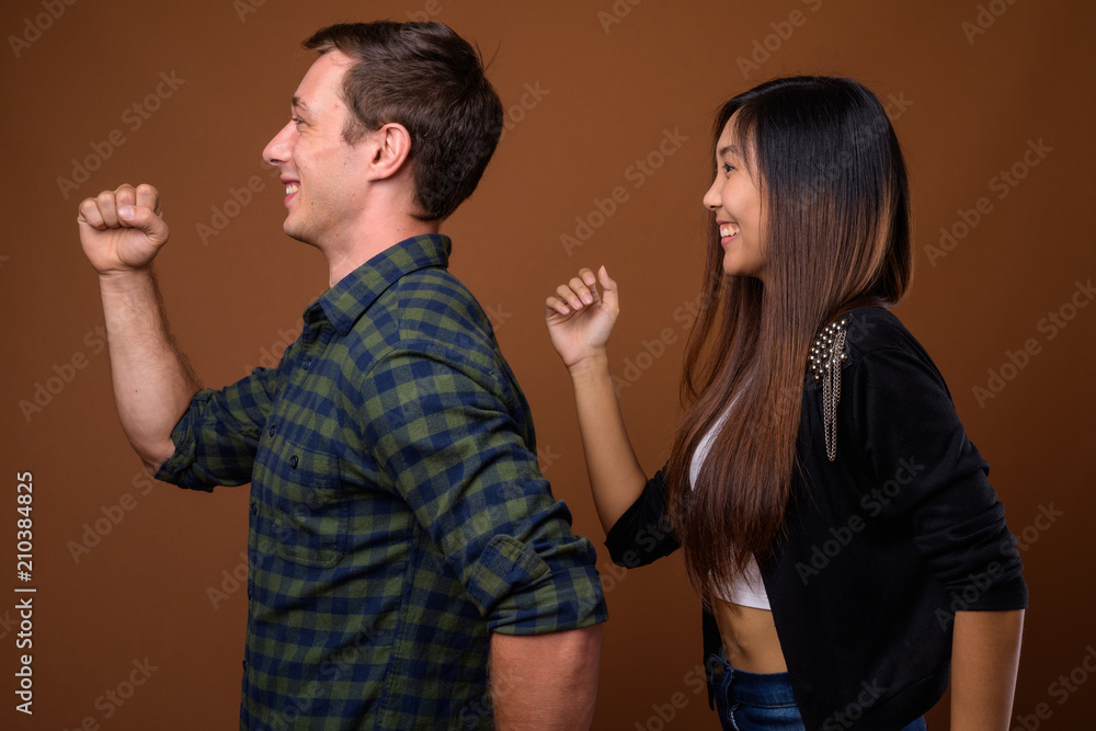 Studio shot of young multi-ethnic couple together against brown Studio shot of young multi-ethnic couple together against brown