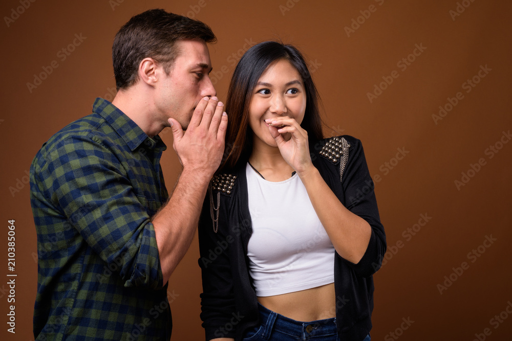 Studio shot of young multi-ethnic couple together against brown Studio shot of young multi-ethnic couple together against brown