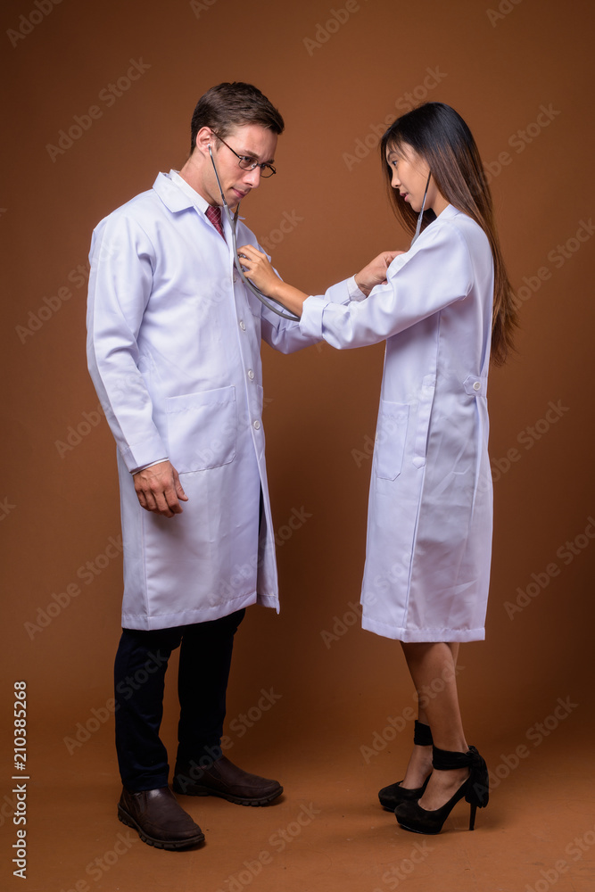 Studio shot of two young doctors together against brown backgrou Studio shot of two young doctors together against brown backgrou