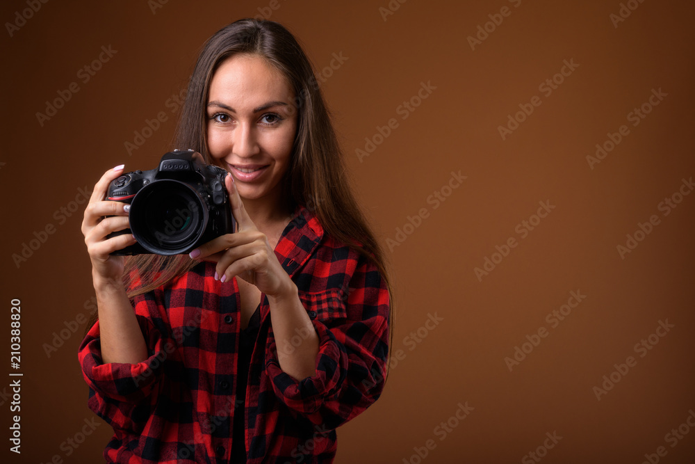 Studio shot of young beautiful woman with camera against brown b Studio shot of young beautiful woman with camera against brown b
