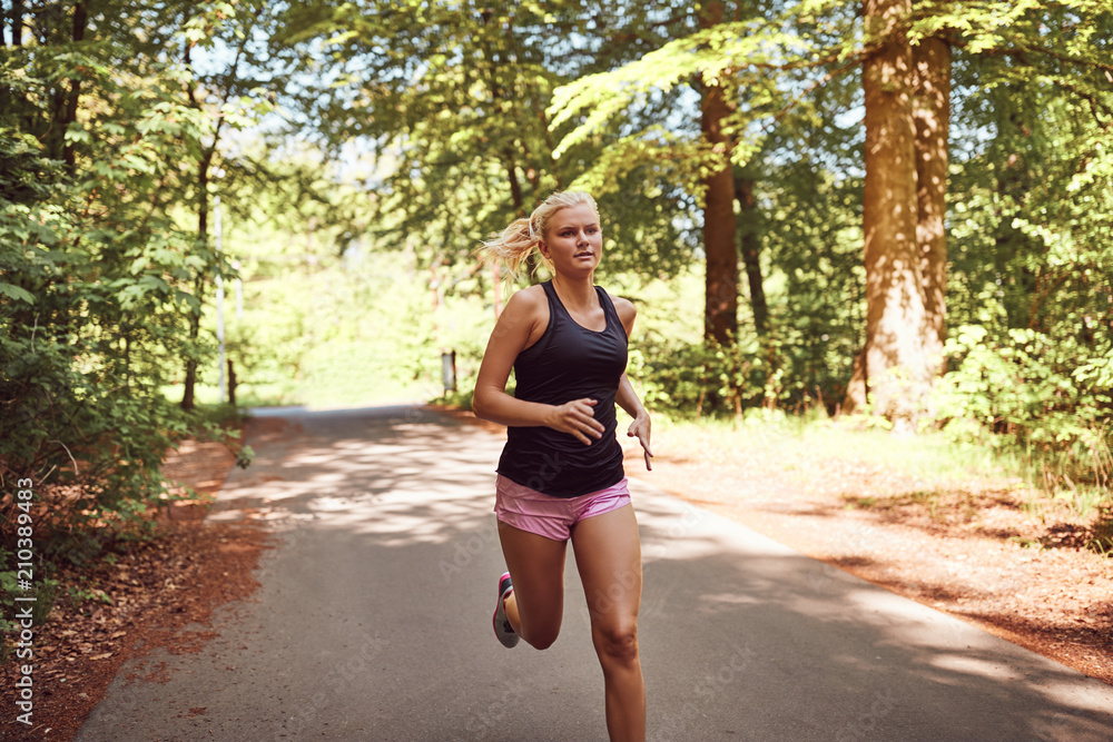 Fit young blonde woman running along a forest path Fit young blonde woman running along a forest path
