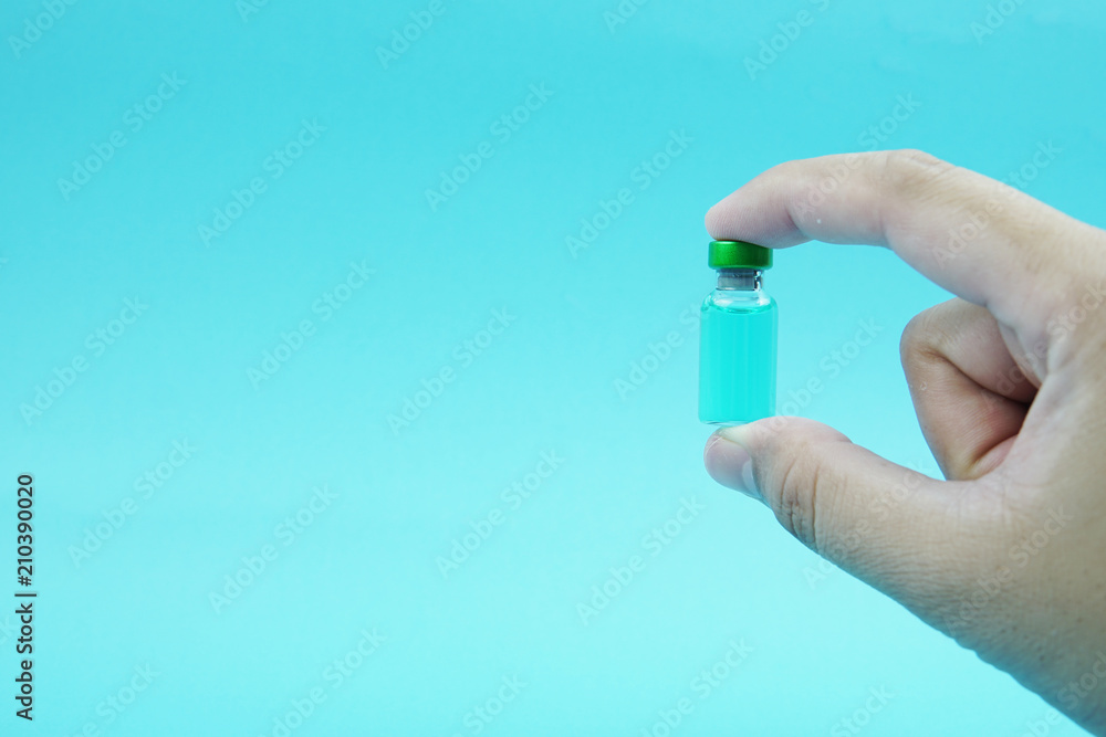 Selective focus a hand holding a vial with blue background. Selective focus a hand holding a vial with blue background.