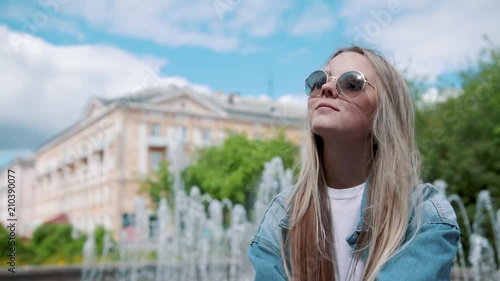 Beautiful young girl sitting on a parapet on the background of the fountain, in a denim jacket photo