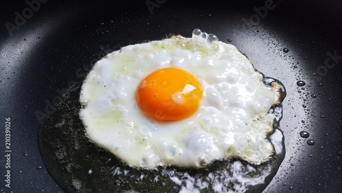 Fried sunny side up egg in a black hot pan.