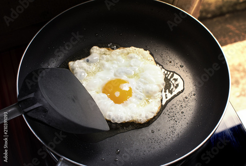 Fried sunny side up egg in a black hot pan and plastic spade at kitchen in home.