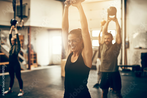 Smiling young woman swinging a dumbbell at the gym photo