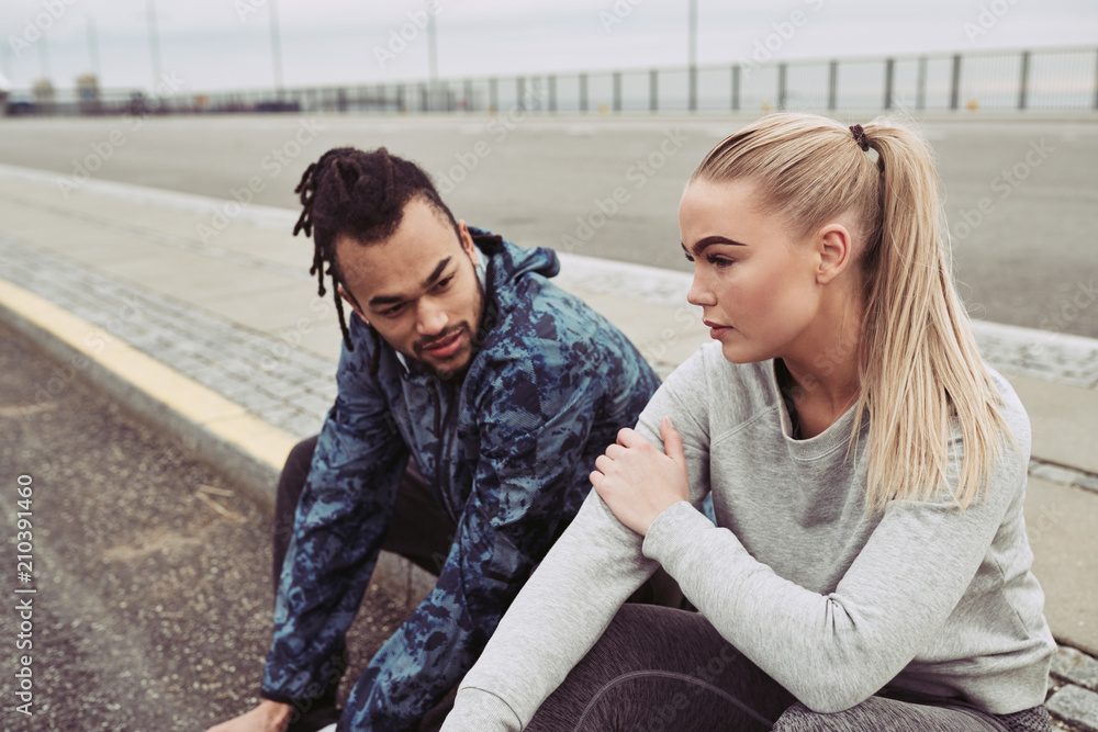 Tired young couple sitting on a road while out running Tired young couple sitting on a road while out running