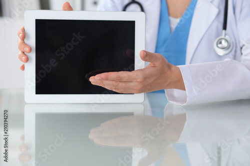 Female doctor using tablet computer while sitting at the workplace, close-up of hands. Medicine, healthcare and help concept