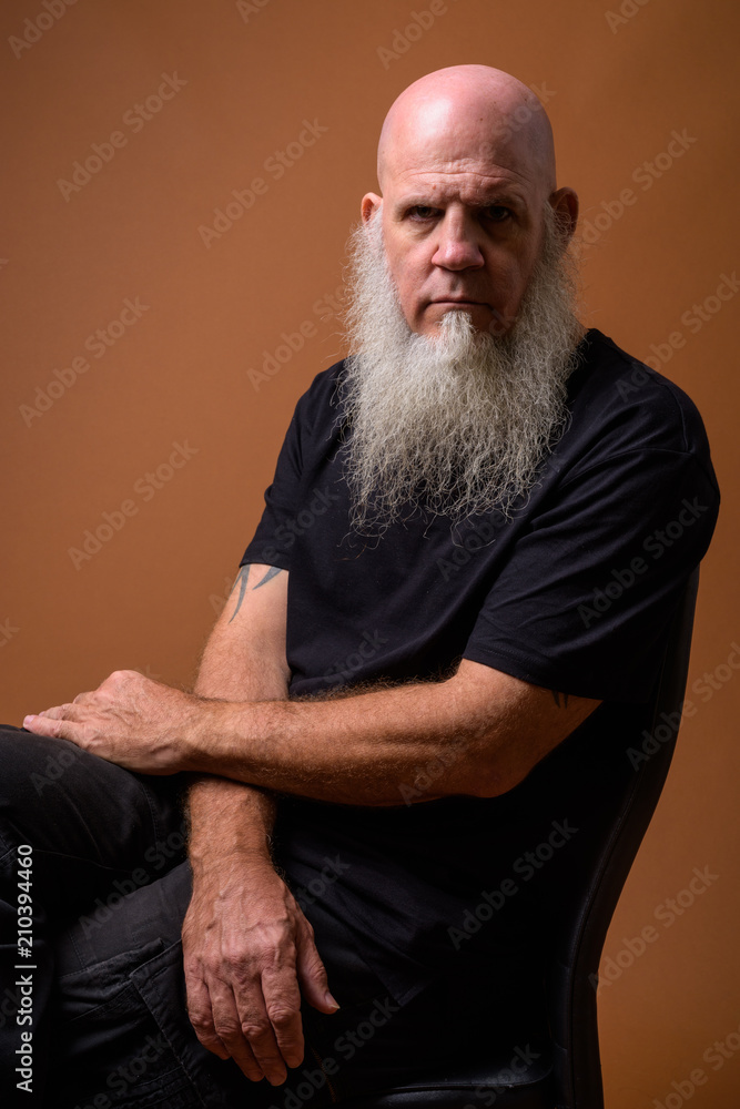 Mature bald man with long gray beard against brown background Mature bald man with long gray beard against brown background