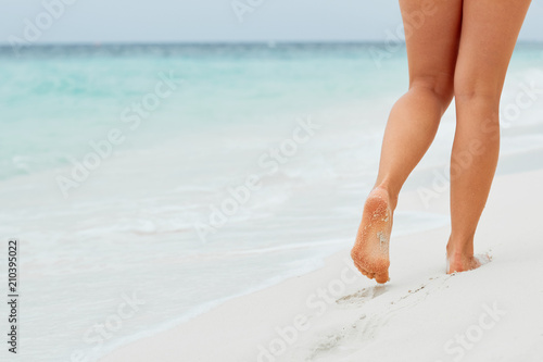 Woman legs and feet walking on the sand of the beach with the sea water in the background. Foot female