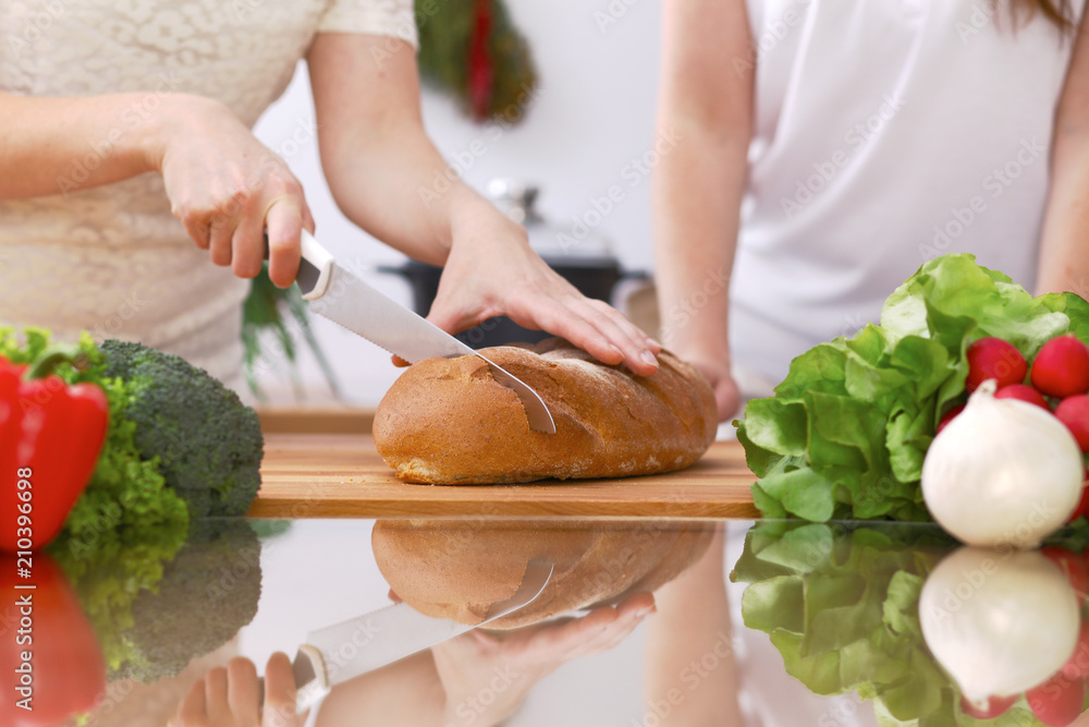 Closeup of human hands cooking in kitchen. Mother and daughter or two female friends cutting bread. Healthy meal, vegetarian food and lifestyle concept Closeup of human hands cooking in kitchen. Mother and daughter or two female friends cutting bread. Healthy meal, vegetarian food and lifestyle concept
