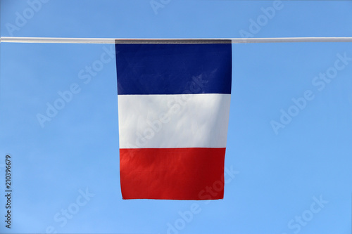 Mini fabric rail flag of France it is a tricolor flag featuring three vertical bands colored blue white and red, hanging on the rope cloth on blue sky background.