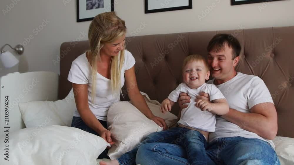 Loving parents play with their son on the bed laughing and smiling in the bedroom Loving parents play with their son on the bed laughing and smiling in the bedroom