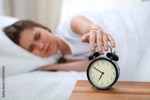 Sleepy young woman stretching hand to ringing alarm willing turn it off. Early wake up, not getting enough sleep concept