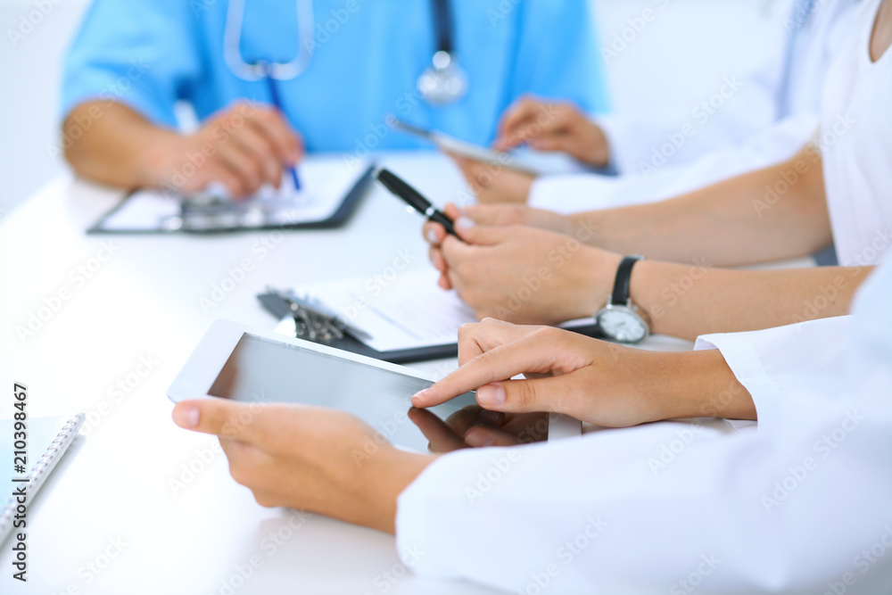 Doctor using tablet computer at medical meeting, closeup. Group of colleagues at the background Doctor using tablet computer at medical meeting, closeup. Group of colleagues at the background