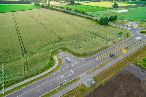 Aerial view of a road with signs and guidelines for traffic between a new development area for an industrial estate and an arable area with green wheat