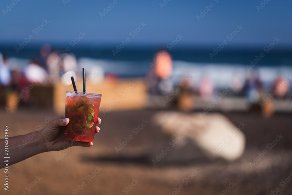 Hand are holding strawberry mojito with sunny coast on background.